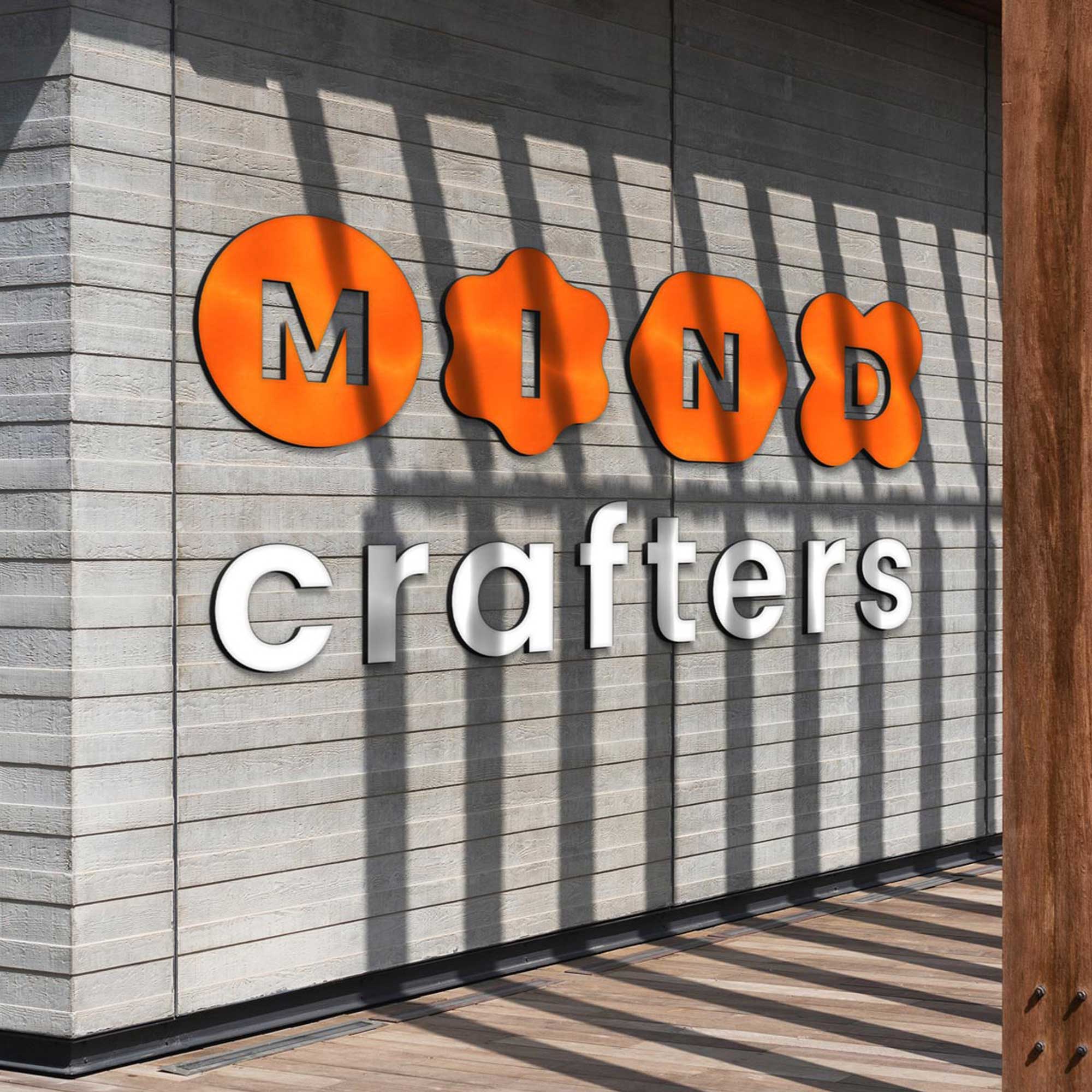 שלט תלת־ממדי צבעוני של המותג Mind Crafters על קיר עץ מודרני, עם אותיות כתומות ולבנות. מיתוג צעיר וחדשני ללמידה טכנולוגית לנוער.